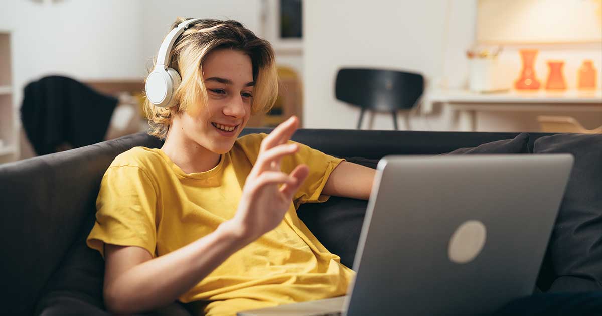 Ein Schüler im gelben T-Shirt sitzt auf dem Sofa mit Kopfhörern auf den Ohren und mit einem Laptop auf dem Schoß.