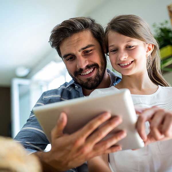 Ein Vater schaut gemeinsam mit seiner Tochter auf ein Tablet und schreiben der Lehrkraft der Tochter.