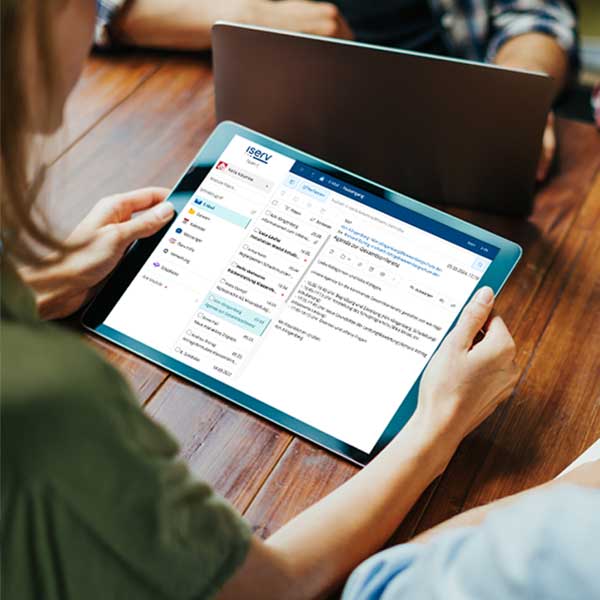 Eine Frau im Anschnitt hält ein Tablet in beiden Händen auf dem das E-Mail-Modul der IServ Schulplattform abgebildet ist.