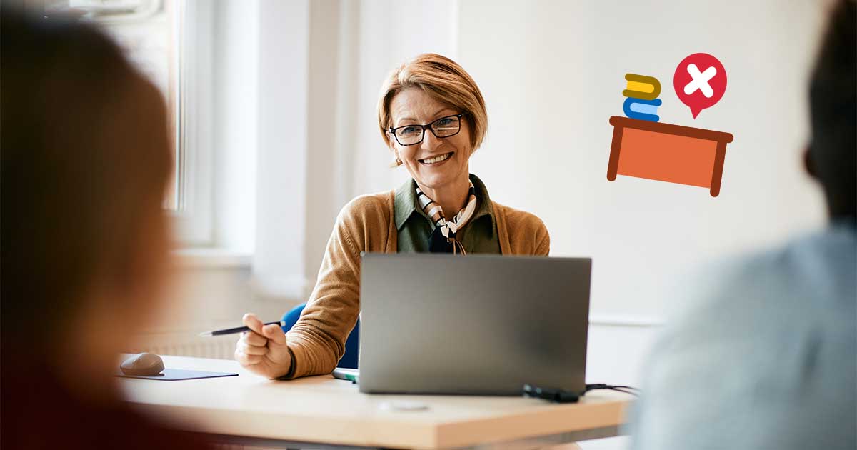 Frau sitzt im Klassenzimmer an einem Tisch mit Laptop