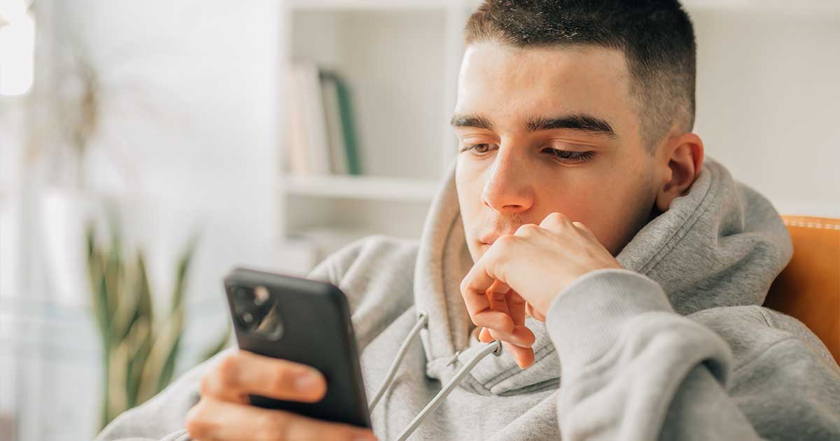 Ein Schüler im grauen Hoodie sitzt und schaut auf sein Smartphone.